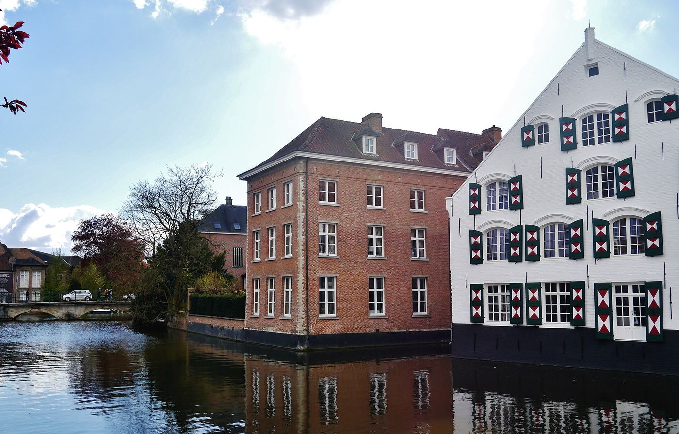 Wit geschilderde gevel met groene luiken en een bakstenen huis aan de Nete in Lier, gespiegeld in het water