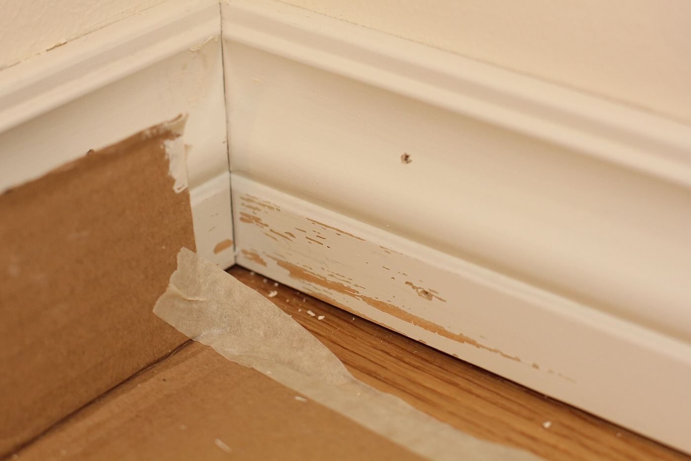 Afplakband langs een witte plint en een houten vloer, na het schilderen van de muur