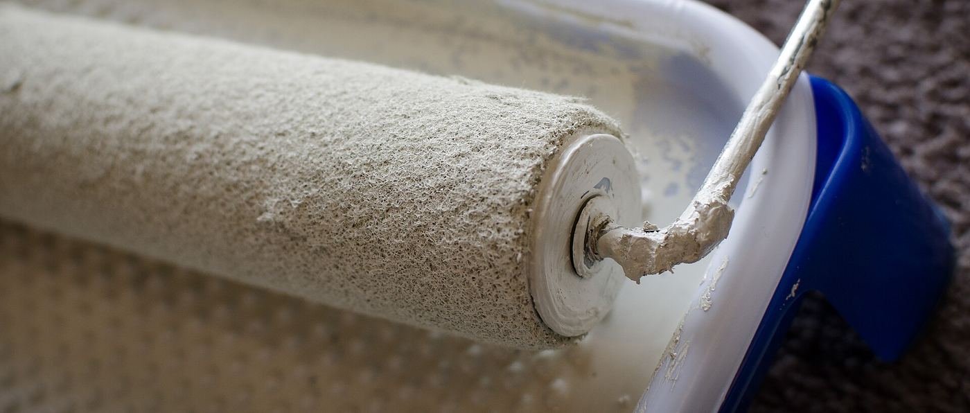 Verfrol met witte verf in een verfbak, van dichtbij
